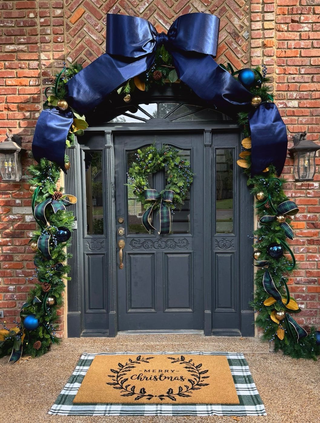 Navy bow and plaid garland framing a Christmas front door
